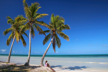 Woman sitting by the palm trees on the coast of Ouvea lagoon on Ouvea Island, Loyalty Islands, New Caledonia - obrazy, fototapety, plakaty