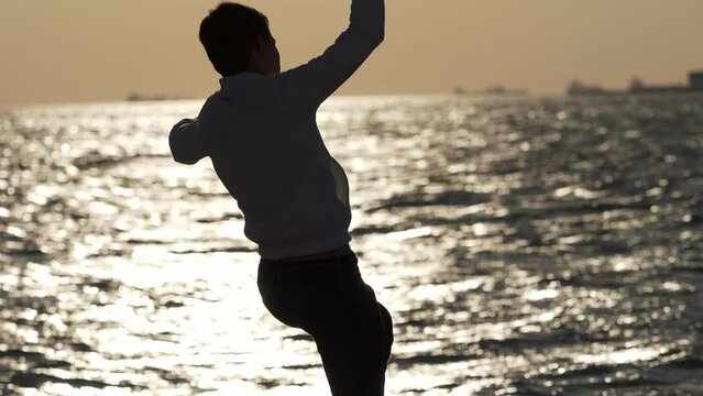 Boy silhouette stands on rocky shore, throws a stone into the sea