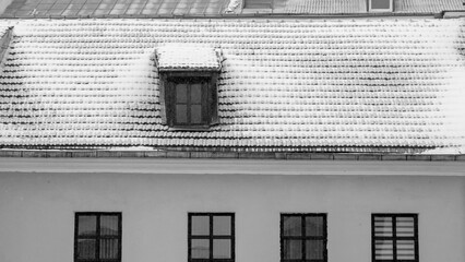 Black and white photo of traditional English house attic with snow on the roof. Copy space. Textured background.