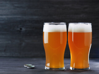 two glasses of beer on a dark wooden background