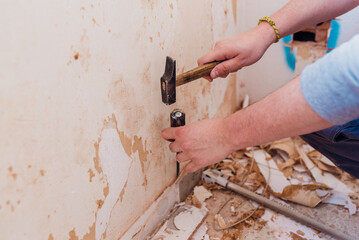 Person removing the skirting board with a hammer and chisel.
