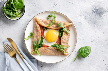 French buckwheat crepe with egg, ham and spinach on gray background. galette bretonne. flat lay...
