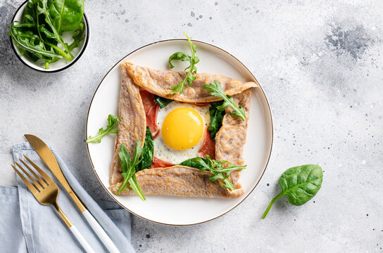 French buckwheat crepe with egg, ham and spinach on gray background. galette bretonne. flat lay with copy space