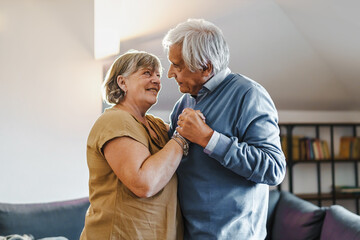 Grandmother and grandfather dancing at home holding hands and looking on each other eye
