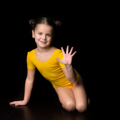 Cute cheerful little girl gymnast sitting on floor