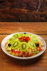 Puff salad with chicken breast, garnished with kivi and olives in a salad bowl on a wooden table.