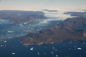 poszarpane surowe i skaliste wybrzeże Grenlandii oraz morze pokryte krą lodową widziane z samolotu z dużej wysokości - 482907666