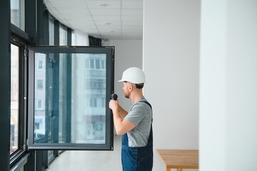 Workman in overalls installing or adjusting plastic windows in the living room at home