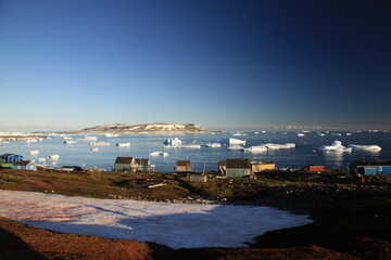 małe czerwone domki w miasteczku u wybrzeży grenlandii oraz morze arktyczne z górami lodowymi i...