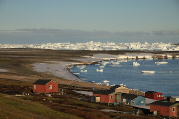 małe czerwone domki w miasteczku u wybrzeży grenlandii oraz morze arktyczne z górami lodowymi i krą w tle - obrazy, fototapety, plakaty