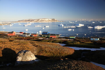 małe czerwone domki w miasteczku u wybrzeży grenlandii oraz morze arktyczne z górami lodowymi i krą w tle - 482908450