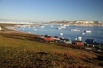małe czerwone domki w miasteczku u wybrzeży grenlandii oraz morze arktyczne z górami lodowymi i krą w tle - 482908483