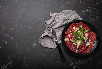 Italian cold meat appetizer Beef carpaccio with parmesan cheese and arugula on black plate with...