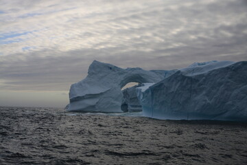 masywna góra lodowa z naturalnie wyżłobionym tunelem u wybrzeży grenlandii - 482908667