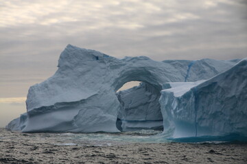 masywna góra lodowa z naturalnie wyżłobionym tunelem u wybrzeży grenlandii - 482908695