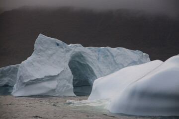 majestatyczna góra lodowa u wybrzeży grenlandii z naturalnie powstałym w niej odłamem w kształcie łuku - obrazy, fototapety, plakaty