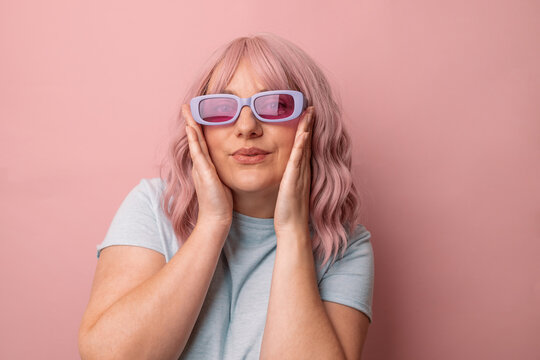 Happy young caucasian woman in bright stylish sunglasses and a blue t-shirt, smiling posing looking at the camera isolated over pink background.