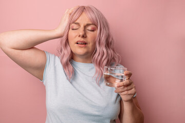 Sick unwell young woman touching head and drinking water while taking painkiller pill against...