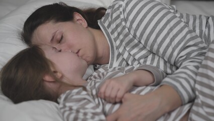 Brunette mother and little child sleep bed together. Mom and daughter lean cheeks hugging tightly. Woman and kid see sweet dreams cozy bedroom. Happy family. Children sleep with plush toy and mommy