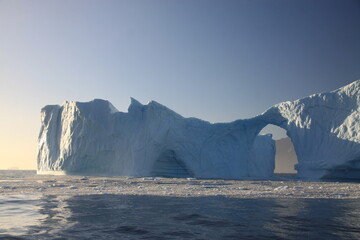 dziura w górze lodowej w kształcie łuku na morzu pokrytym krą w słoneczny dzień - obrazy, fototapety, plakaty