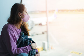 A young girl tourist in a protective mask and with backpack looks out the window at the departing planes. The girl is waiting for her flight. Travel concept. Copy space.
