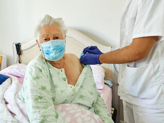 Senior adult elderly caucasian woman receives Covid-19 vaccine at home from doctor