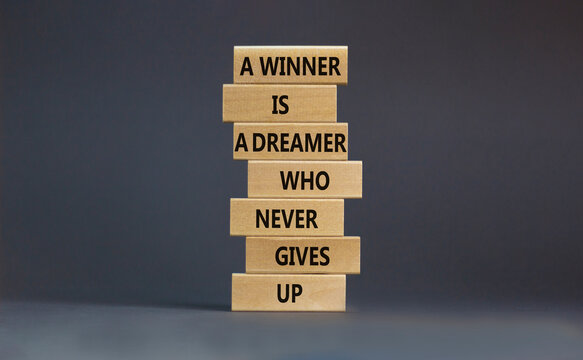 Winner or dreamer symbol. Wooden blocks with words A winner is a dreamer who never gives up. Beautiful grey table, grey background, copy space. Business, winner or dreamer concept.
