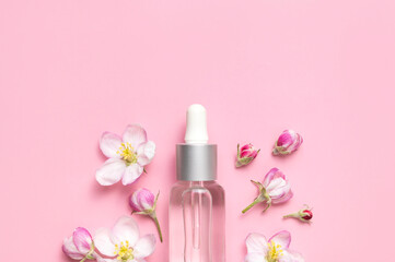 Clean glass cosmetic bottles with dropper, delicate spring flowers on pink background flat lay top view. Spring concept of natural organic cosmetics, beauty herbal product spa aroma oil. Mockup