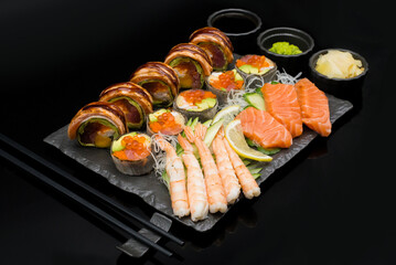 Sushi rolls set served on black stone slate on dark background