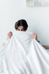 brunette man looking at camera while obscuring face with white blanket.