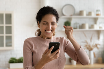 Young Hispanic woman hold smartphone enjoys good news read on internet, looks at cellphone screen feels happy, get great commercial offer, long awaited call, watch lottery result celebrate win concept