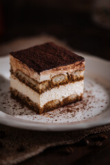 Tiramisu cake dessert served with coffee, biscuit and cocoa as ingredients on a bright white background. One piece