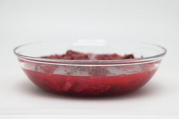 Red flavored fresh borscht soup in transparent brown tempered glass plate with handles, metal steel spoon with patterns on board against background green grass, light day summer sun, selective focus. - Powered by Adobe