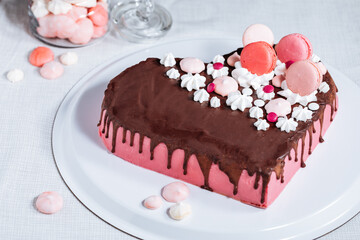 Pink heart shaped cake with chocolate glaze, meringues and macaroons on top as decoration. Placed on white plate. Valentine's day, mothers day, birthday, celebration concept.