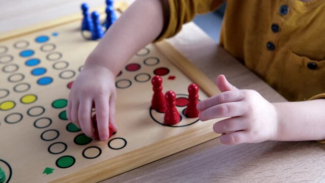 close-up of hands of small child manipulate with wooden figurines of family board game, smart kid, 2-year-old girl is learning to count, Cross and circle game Parcheesi, foreground focus