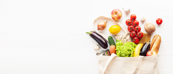 Cotton grocery tote bag with fresh vegetables, fruits, baguette and canned good on wooden background. Healthy food shopping, eco-friendly concept. Flat lay, copy space.