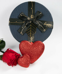 Caja de regalo azul con lazo acompañado de rosa y corazones rojos sobre fondo blanco