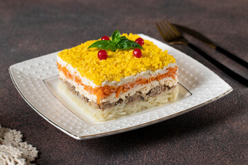 Traditional Russian salad Mimosa with canned fish, potatoes, cheese, carrots and eggs on brown background