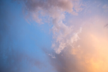 Dramatic moody sunset landscape with puffy clouds lit by yellow setting sun and blue sky.