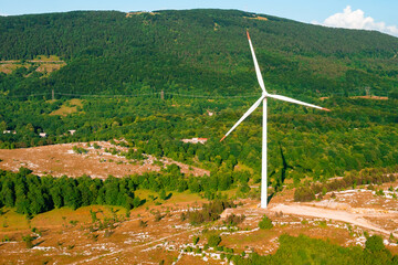 Modern wind driven generator operates producing green energy against big forestry mountain in...