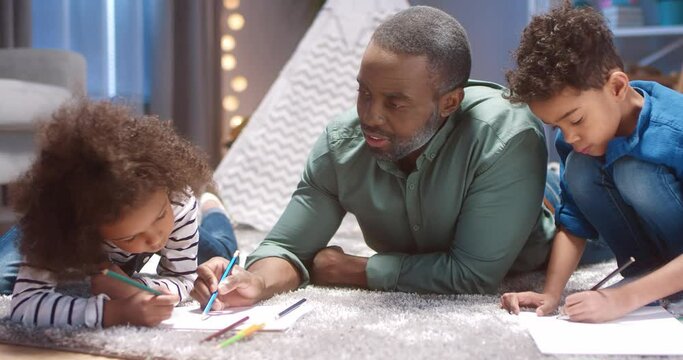 Happy African American family: two grandchildren and grandfather spend free time lying on the floor and drawing pictures.