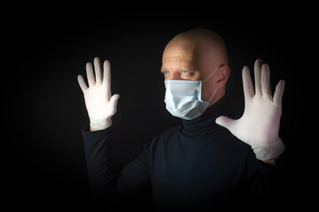 A man in a medical mask and gloves raised his hands up, black background. Prevention and...