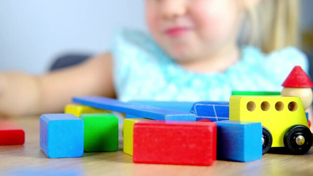 close-up of children's educational toys in hands of toddler, small child, a 2-year-old girl builds houses for characters from color blocks, concept of childhood, earlier child development, creativity