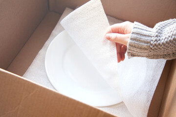 Woman packing white dishes away with white foam sheets