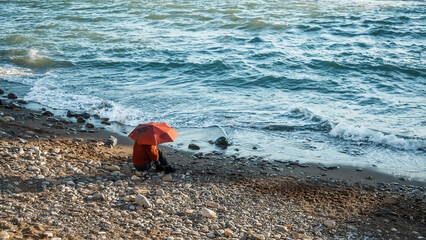 Obraz premium A girl with a red umbrella is sitting on the coast. The Black Sea coast.