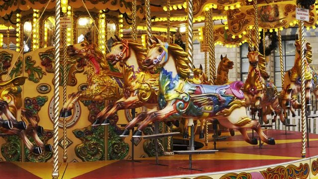 Fairground Vintage Carousel. Bright red and golden carousel with horses and bright glowing lights turning around without passengers in daylight. London Fairground
