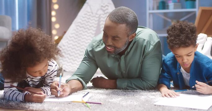 Close up of happy african american grandfather spending weekend with two grandchildren and helping little girl draw picture.