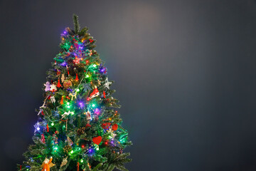 A decorated Christmas tree with a garland and wooden toys stands in the room on a dark blue background of the living room. Space for text. Copy space