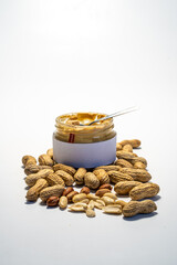 peanut butter in an open glass on a white background, next to scattered peanuts