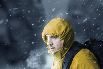 hiker with yellow jacket breathing out in front of blurry mountain landscape